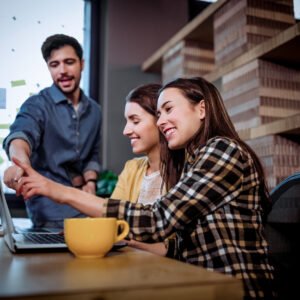 Coworkers smiling while pointing at laptop on desk in creative office